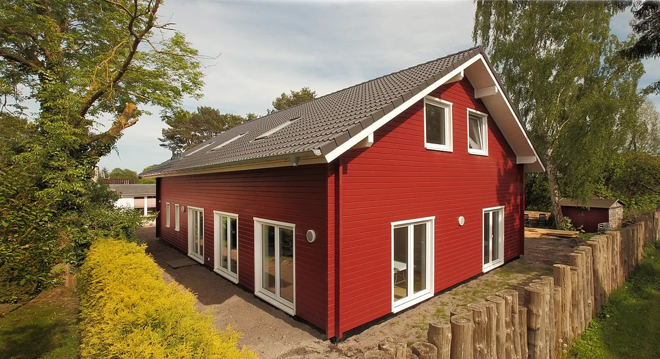 Modernes rotes Holzhaus mit mehreren Fenstern und grauem Ziegeldach in naturnaher Umgebung mit Bäumen und Zaun in Prerow