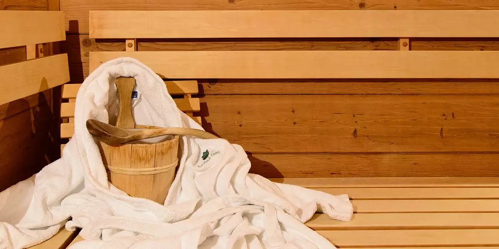 Sauna mit weißem Bademantel und Holzeimer mit Kelle auf einer Holzbank im Steinbach-Hotel im Berchtesgadener Land