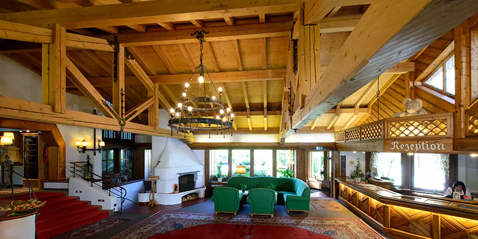 Gemütliche Hotellobby mit Holzbalken, grünen Sitzmöbeln, Kamin, stilvollem Kronleuchter und Rezeption im Steinbach-Hotel im Berchtesgadener Land