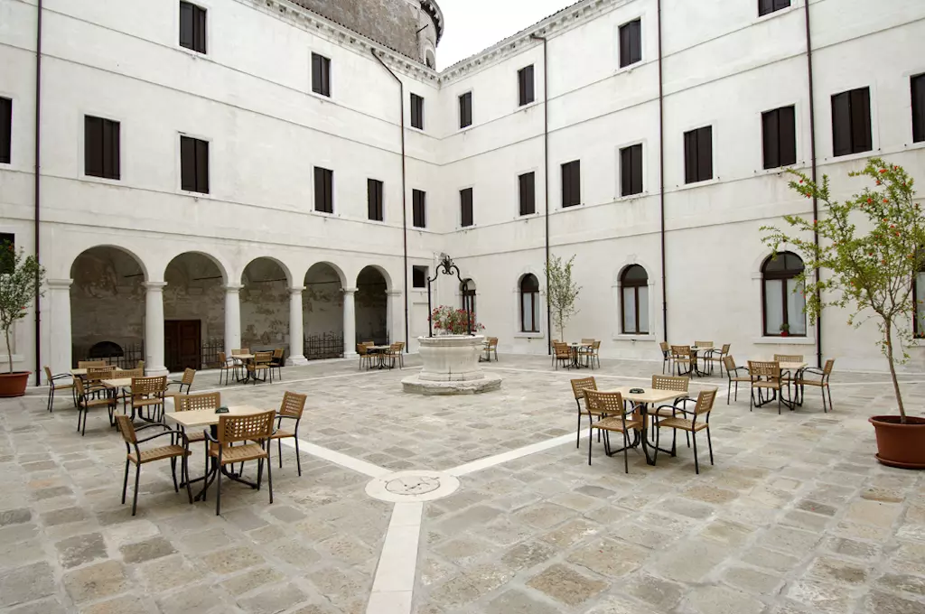 Historischer Innenhof mit Sitzbereich in Venedig, Italien Innenhof eines historischen Gebäudes mit Tischen und Stühlen, umgeben von weißen Fassaden und Arkadengang