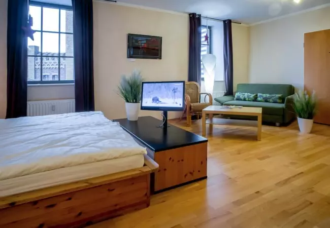 Modern eingerichtetes Hotelzimmer mit Bett, Sofa, Fernseher, Holzboden und großen Fenstern im Hotel Birschel-Mühle in Hattingen