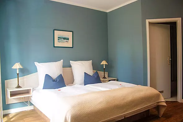 Gemütliches Hotelzimmer mit Doppelbett, blauen Wänden, zwei Nachttischlampen und Holzboden im Hotel Haus Kranich in Prerow