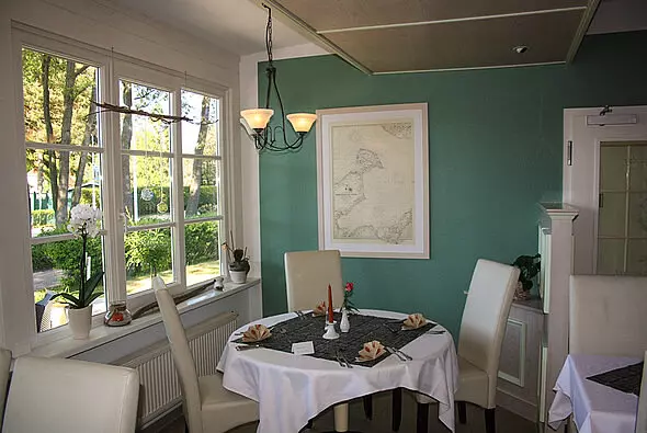 Gemütlicher Gastraum im Hotel Haus Kranich Prerow mit gedecktem Tisch, bequemen Stühlen und großem Fenster mit Blick ins Grüne