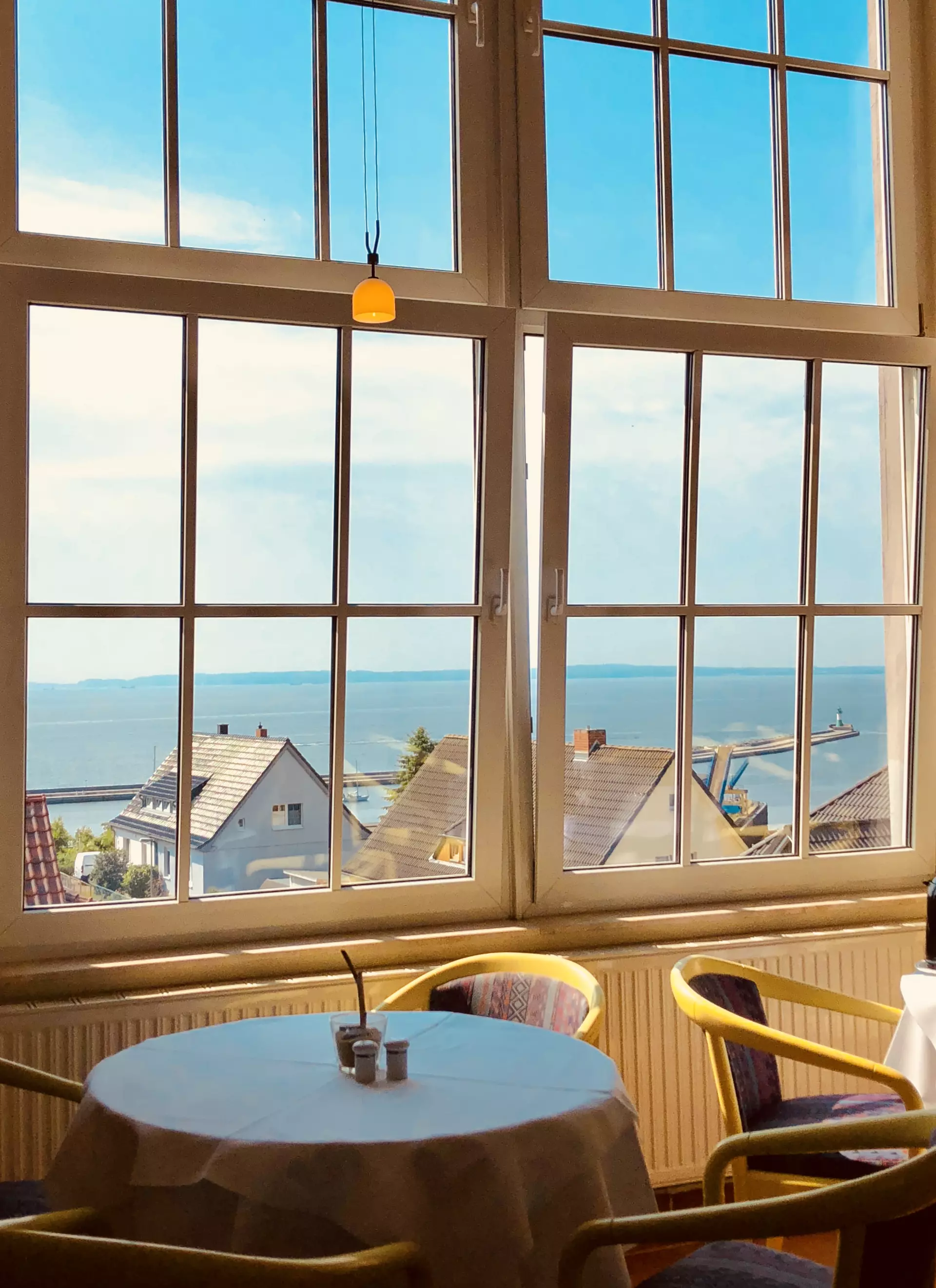 Tisch mit Stühlen vor großen Fenstern mit Blick auf Dächer, Hafen und Ostsee in Kurhotel Sassnitz auf Rügen