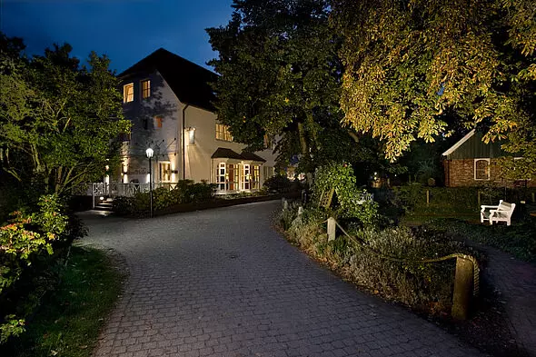 Lichtbeleuchtetes Hotel Inselfriede bei Nacht mit gepflastertem Weg und umgebenen Bäumen auf der Insel Spiekeroog