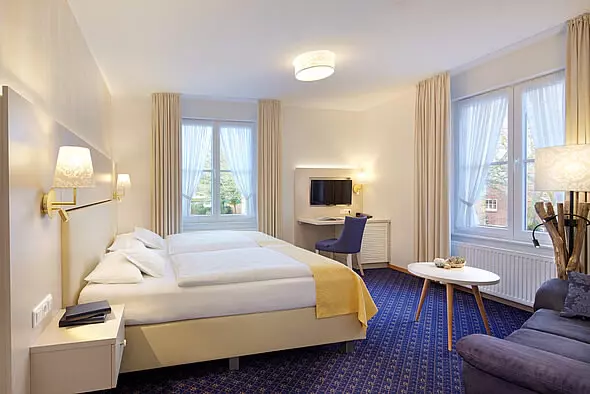 Modern eingerichtetes Hotelzimmer in Hotel Inselfriede Spiekeroog mit Doppelbett, Schreibtisch, Fernseher und großem Fenster mit Vorhängen