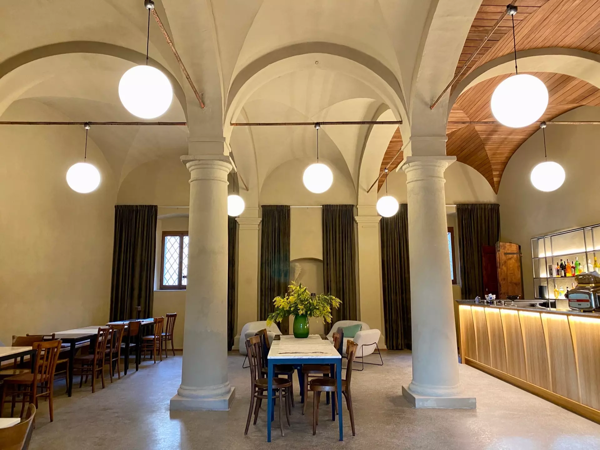 Großräumige Lounge mit Toskanaflair Historischer Innenraum einer toskanischen Unterkunft mit Säulen, gedeckten Tischen, Stühlen und modern beleuchtetem Barbereich