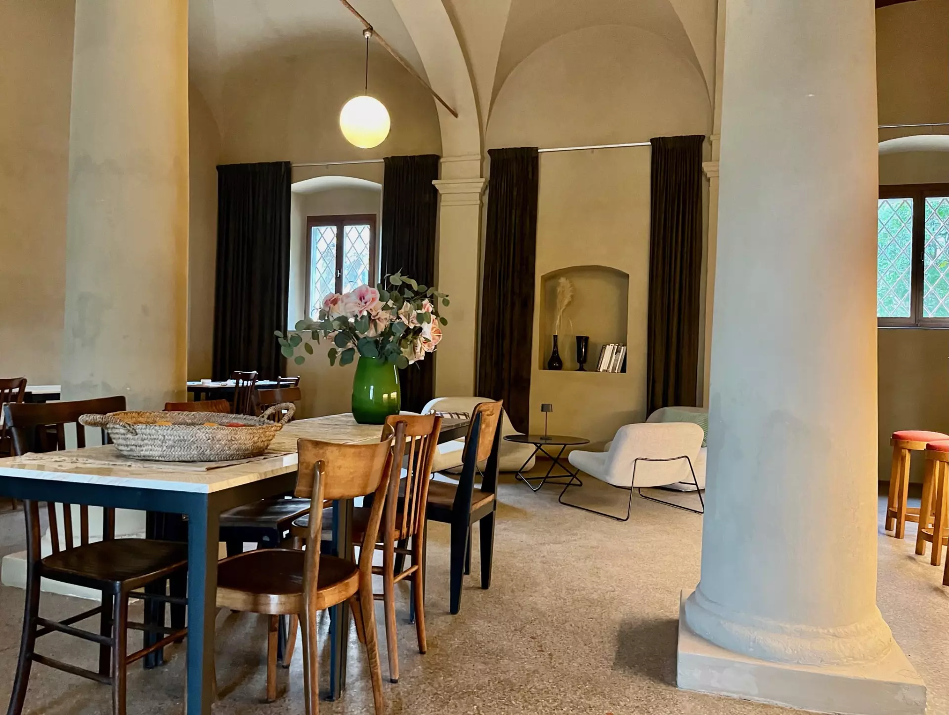 Lounge zum zusammenkommen Essbereich mit Holztischen, Stühlen und Blumendeko in einer ruhigen, hellen Unterkunft in der Toskana mit gewölbten Decken und großen Säulen