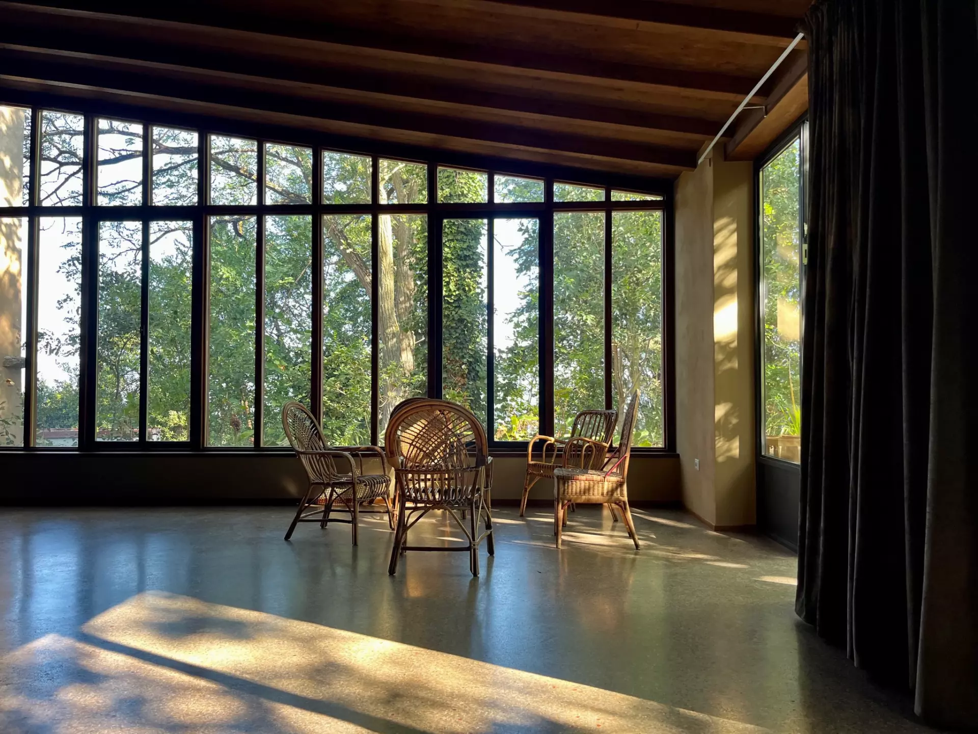 Atelier Ansicht 1 Rattanstühle in einem lichtdurchfluteten Raum mit großen Fenstern und Blick auf Bäume, Unterkunft in der Toskana