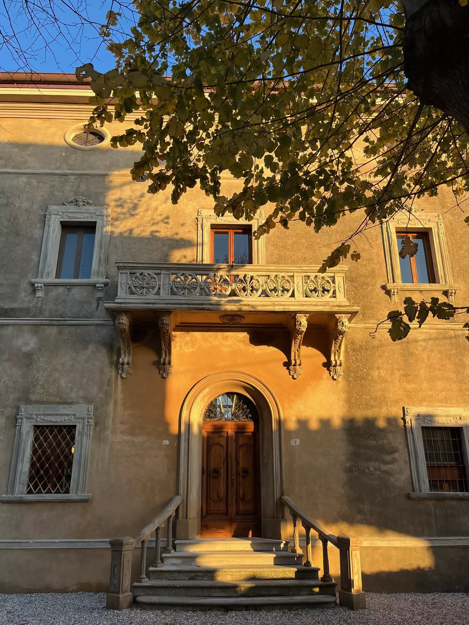 Ansicht von Außen Historisches toskanisches Gebäude mit Holztür, Balkon, mehreren Fenstern und Baum im Vordergrund bei Sonnenuntergang