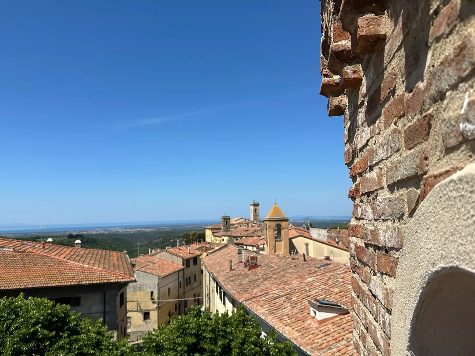 B&B Außenansicht Blick über Dächer und Kirchtürme eines toskanischen Dorfes unter strahlend blauem Himmel mit altem Backsteinmauer im Vordergrund