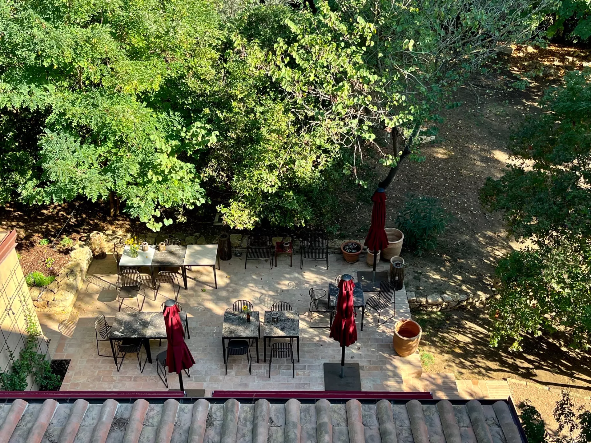 Blick auf die Terasse Terrassenbereich mit Tischen, Stühlen und geschlossenen roten Sonnenschirmen umgeben von grünen Bäumen in der Unterkunft Toskana