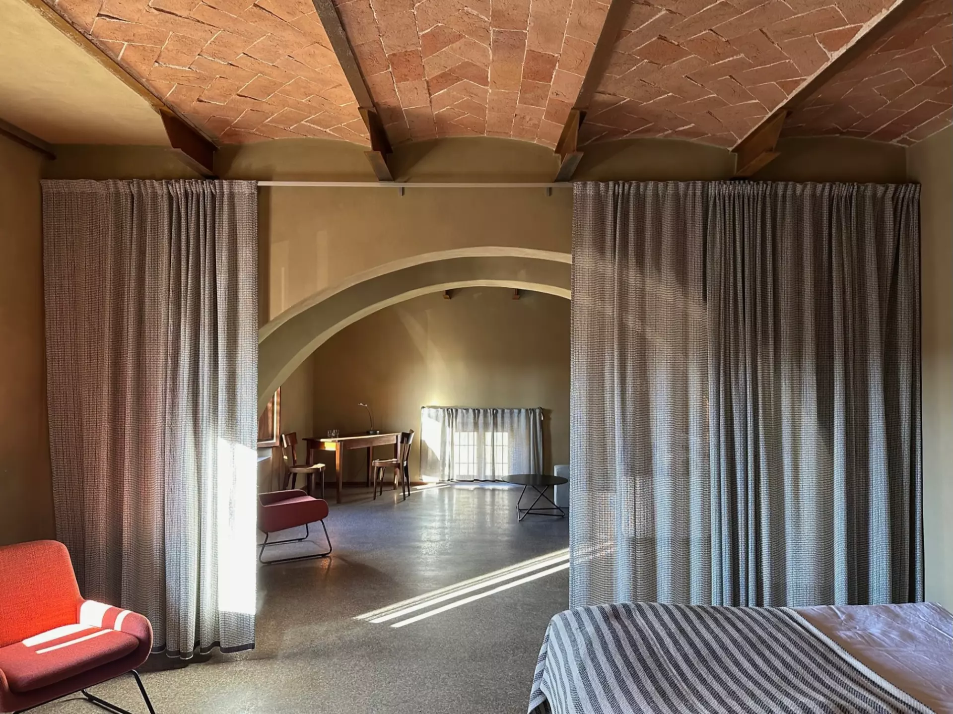 Helles Zimmer der Unterkunft Toskana mit gemütlichem Bett, roten Sesseln, Vorhängen und sichtbaren Backsteinbögen an der Decke