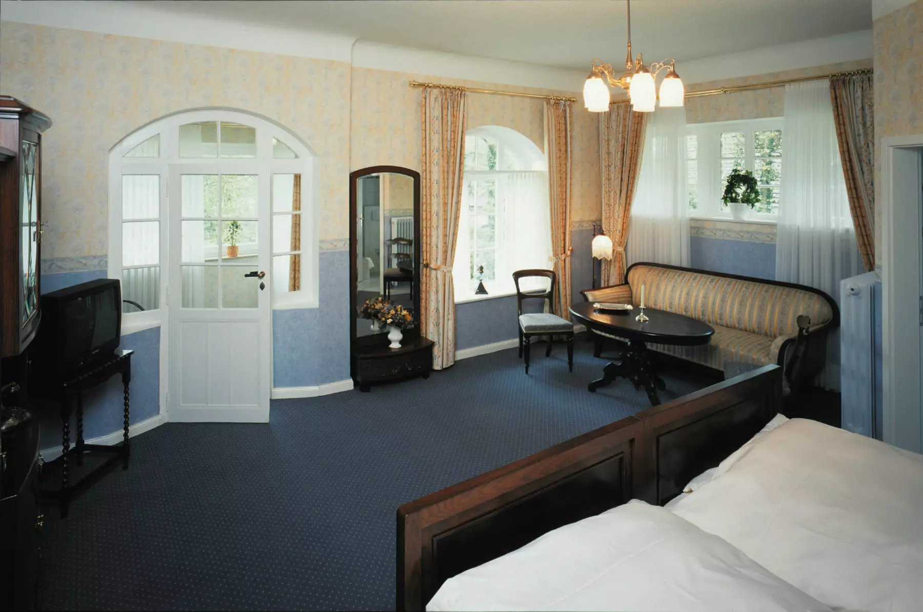 Hotelzimmer im Hotel Buchenhof Worpswede mit Doppelbett, antiken Möbeln, Sofa, Tisch, Stühlen und nostalgischem Fernseher