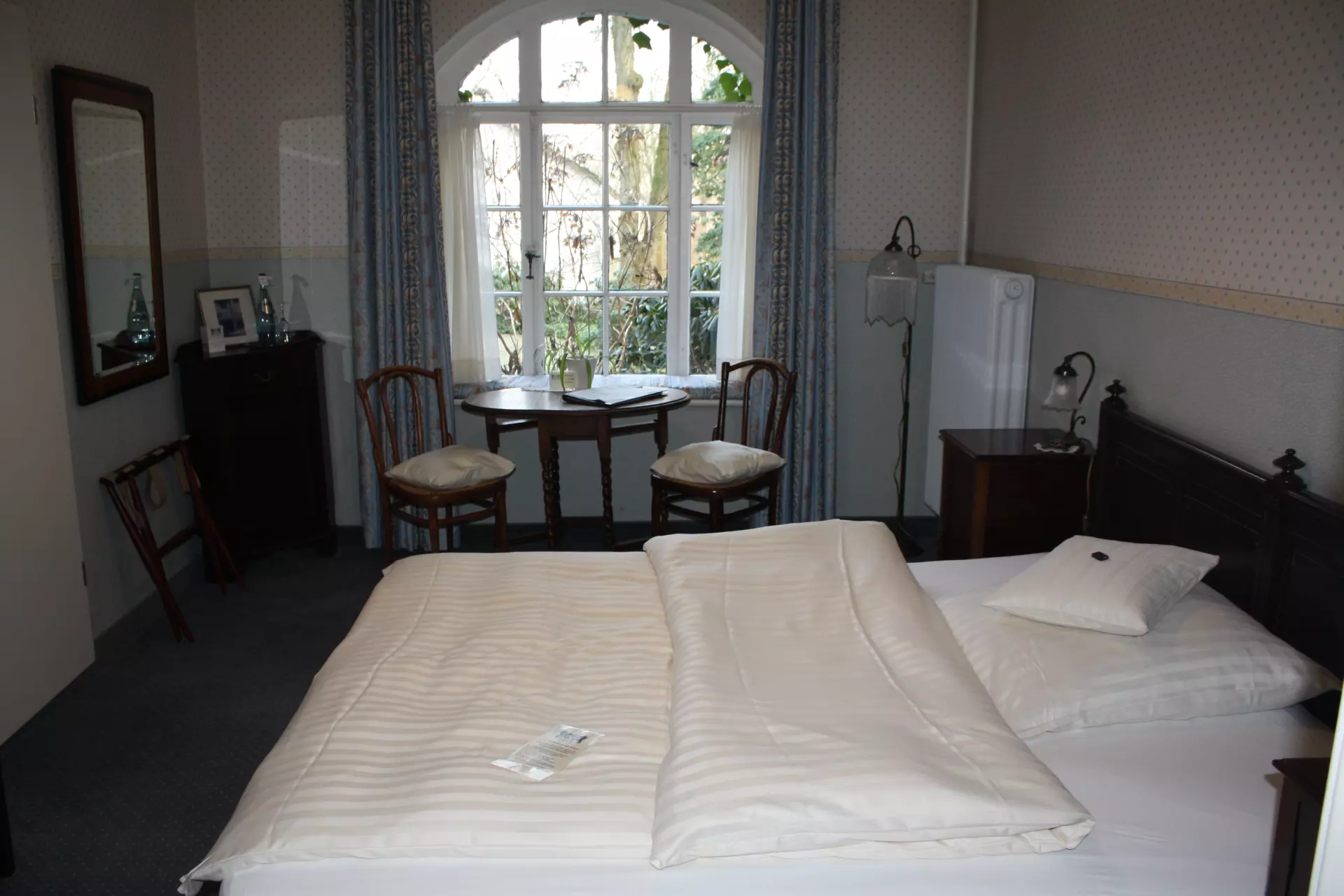 Gemütliches Hotelzimmer im Hotel Buchenhof Worpswede mit großem Doppelbett, Fenster mit Blick auf Garten und kleinem Sitzbereich mit Tisch und Stühlen