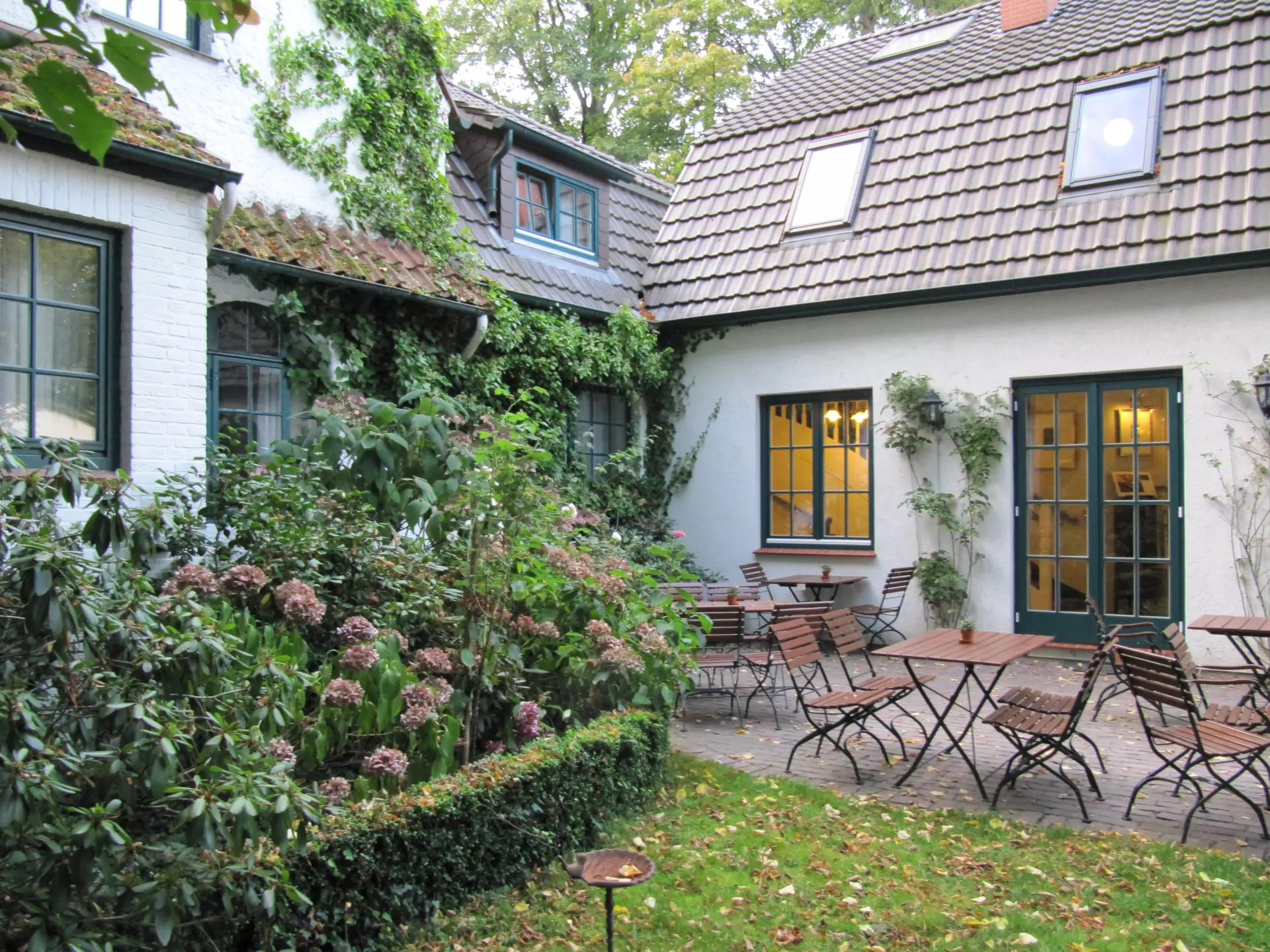 Innenhof mit Gartenterrasse und Sitzgruppen vor einem begrünten Hotelgebäude des Hotel Buchenhof in Worpswede