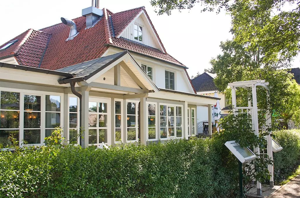 Hotel Haus Kranich in Prerow mit weißem Wintergarten, rotem Dach und grüner Hecke bei sonnigem Wetter