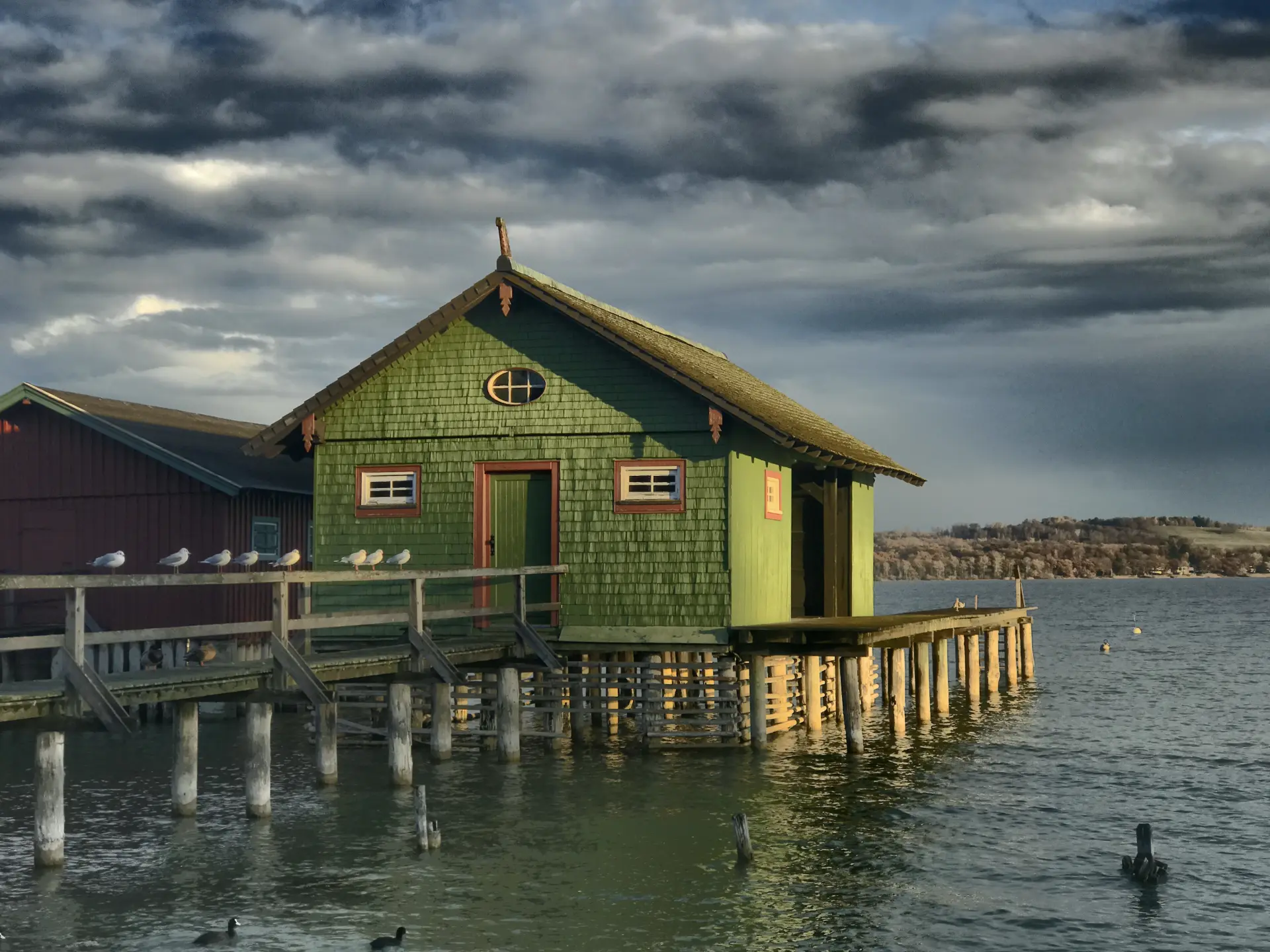 Grünes Haus auf Stelzen am Wasser unter dramatischem Himmel, Licht und Perspektive betont, Foto von Christian Frank mit klarer, atmosphärischer Komposition