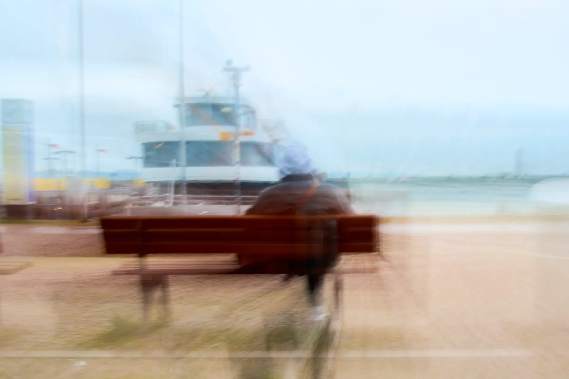 Verschwommene Sitzbank mit Person vor Hafen und Schiff in experimenteller ICM-Fotografie von Christian Frank, die Bewegung und Atmosphäre im urbanen Raum betont