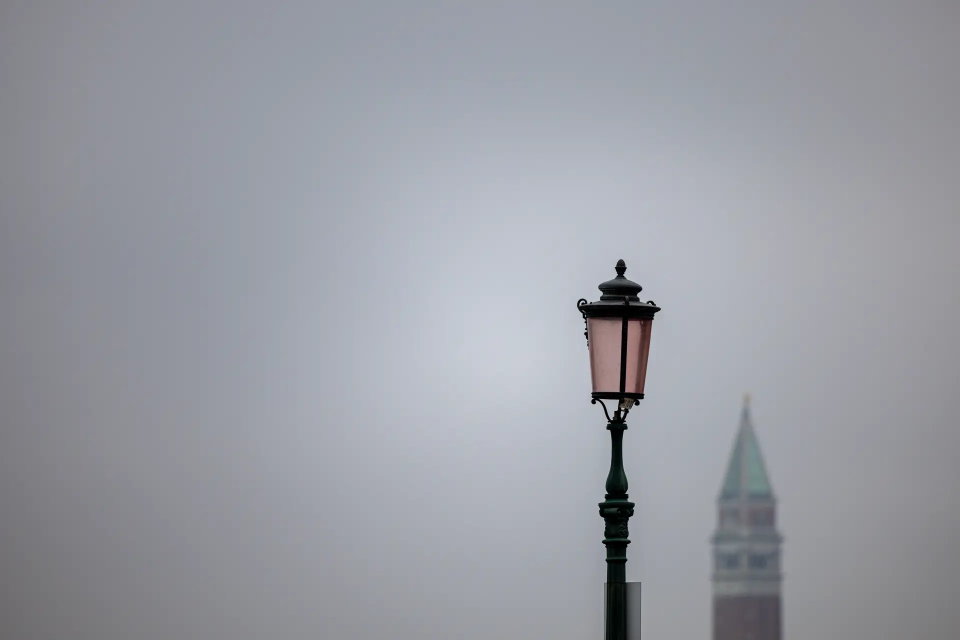 Minimalistische Straßenlaterne vor unscharfem, nebligem Hintergrund mit Turmspitze, fotografiert von Urs Renggli mit klarer, meditativer Bildwirkung