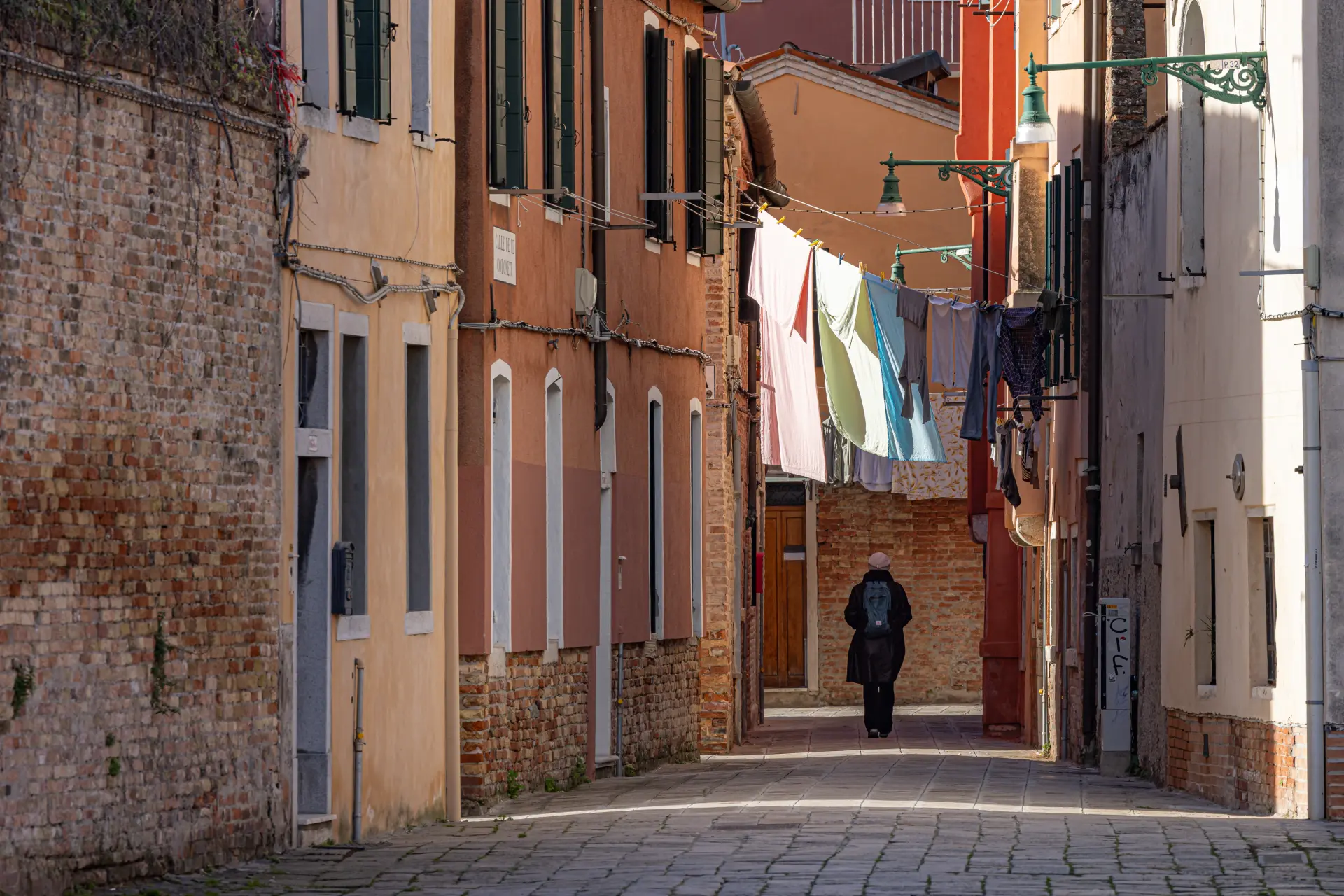 Enge Gasse mit Waschwäsche über Kopf und einer Person im Schatten, minimalistisch komponiert von Urs Renggli mit ruhiger Lichtstimmung und reduzierter Farbpalette