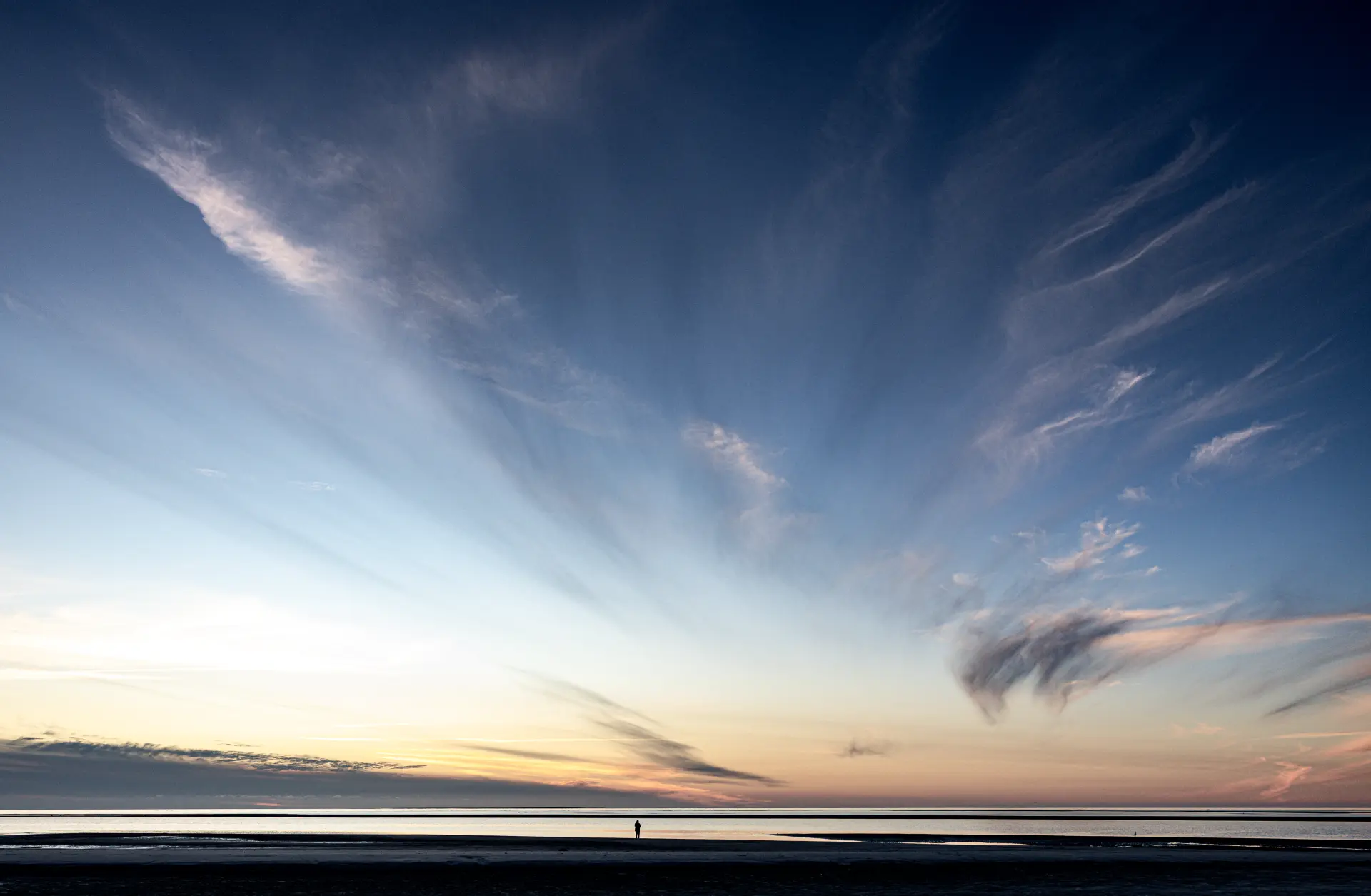 Weiter Küstenstrand bei Sonnenuntergang mit sanften Wolkenformationen und ruhiger Meereslinie von Urs Renggli minimalistischer Naturfotografie