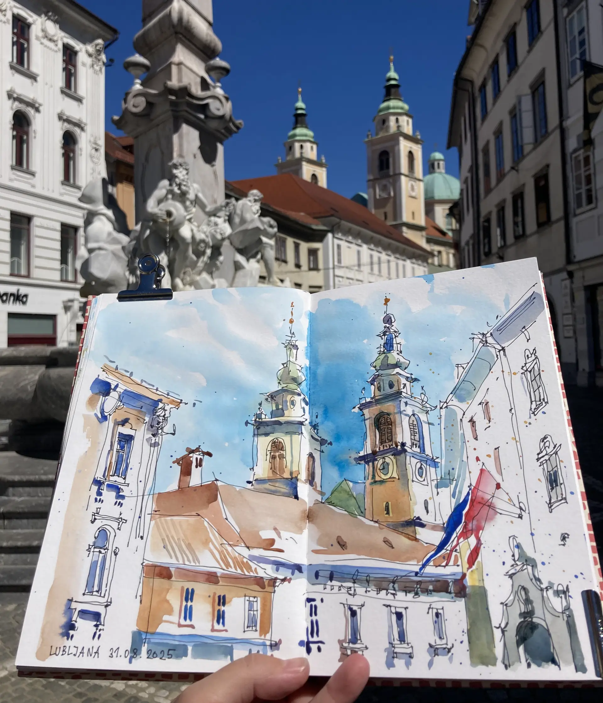 Janna Liebender Folz Skizzen Lübljana Aquarellskizze von Janna Liebender-Folz zeigt en plein air lebendige Stadtansicht mit Kirchtürmen und historischen Gebäuden in leuchtenden Farben und dynamischer Wasserzeichnung