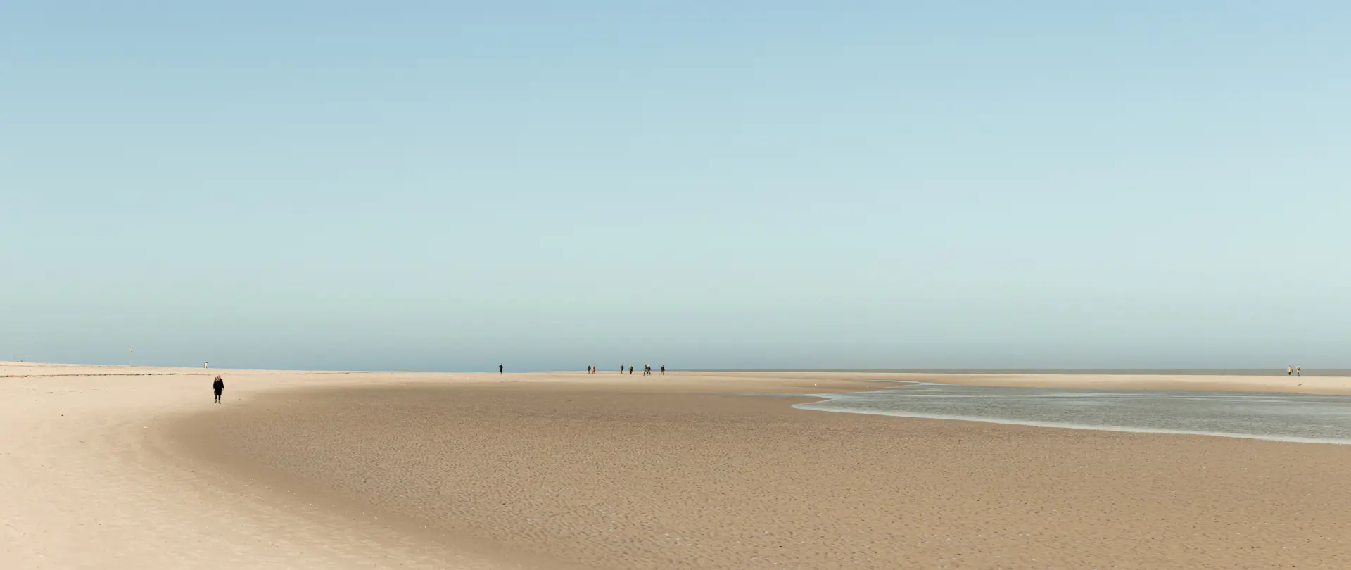 Weiter Küstenstreifen mit minimalistischem Sand und wenigen Personen, eingefangen in ruhiger, diffuser Lichtstimmung von Urs Renggli