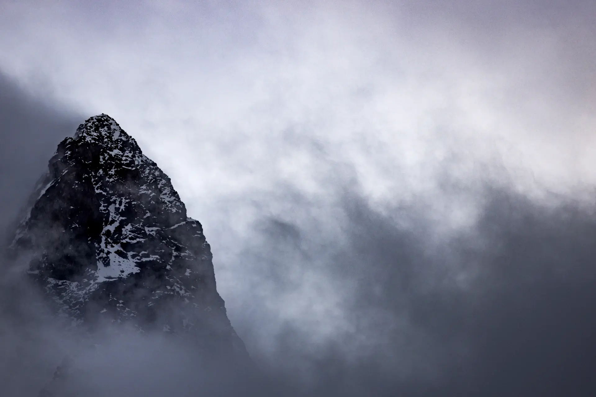 Schroffes Bergmassiv mit Schneeresten in diffuser Nebelstimmung, Minimalismus und Ruhe vereint in Urs Rengglis präziser Naturfotografie