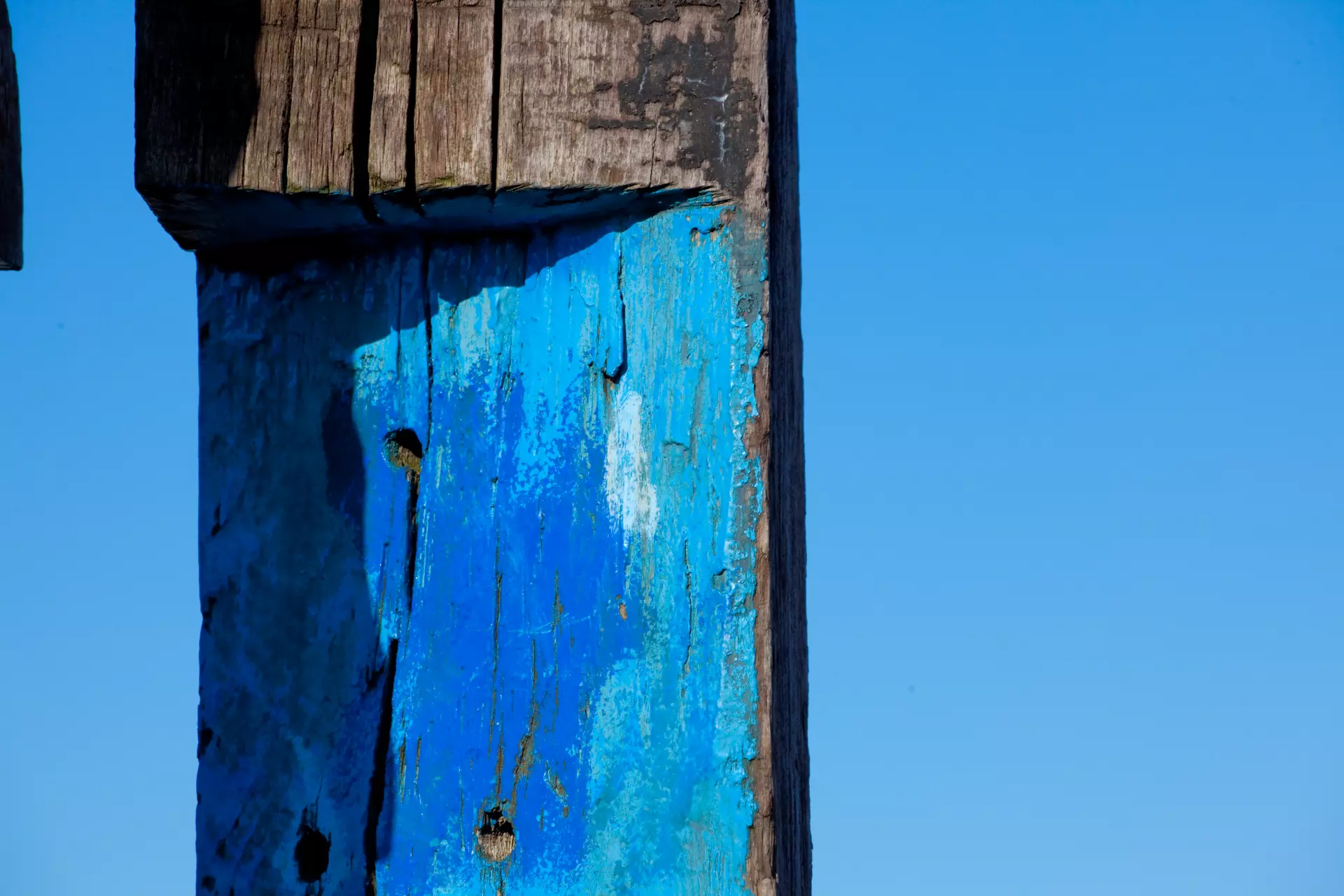 Blaue Farbe auf Holz Abgeblätterte blaue Farbe auf einem hölzernen Pfahl vor blauem Himmel – Texturfotografie von artistravel Dozent Uwe Schmid