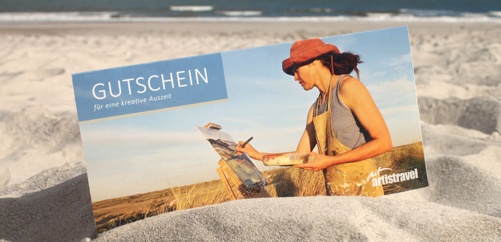 Ein artistravel-Gutschein steckt im Sand am Strand 