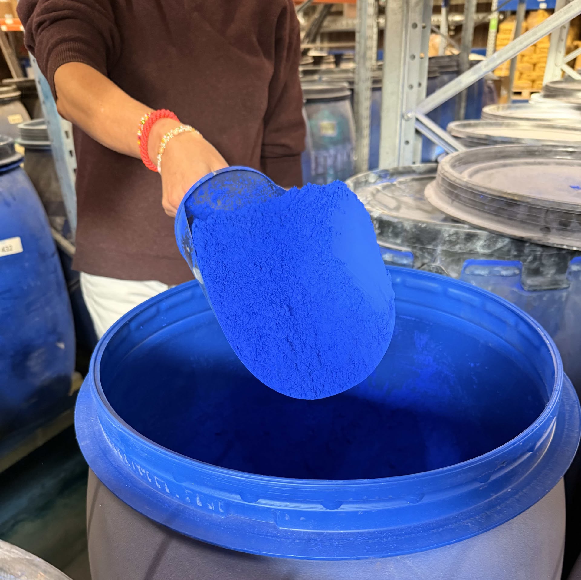 Eine Frau steht hinter einem Fass mit blauem Farbpigment und hebt eine Schaufel mit Pigment darauf heraus.