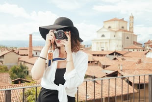 Besondere Fotos machen lernen im Fotokurs. Foto: SplitShire/Pixabay License. Eine Frau mit einer Kamera in den Händen vor einer bebauten Kulisse.