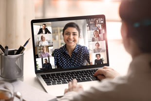 "© fizkes / Adobe Stock” Blick über die Schulter einer Frau, auf ihrem Laptop ist eine Video-Konferenz geöffnet
