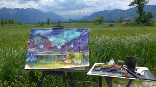 Bei dem Bild handelt es sich um eine Kursimpression von Jutta Höfs. Vor einer Wiese mit Blick auf die Berge ist eine Staffelei aufgebaut.