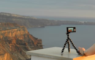 Fotografieren lernen im Fotokurs - Reisefotografie. Foto: Jutta Engelage. Eine Fotografie von Jutta Engelage, die eine Kamera auf einem Stativ vor eine Kulisse am Meer präsentiert.