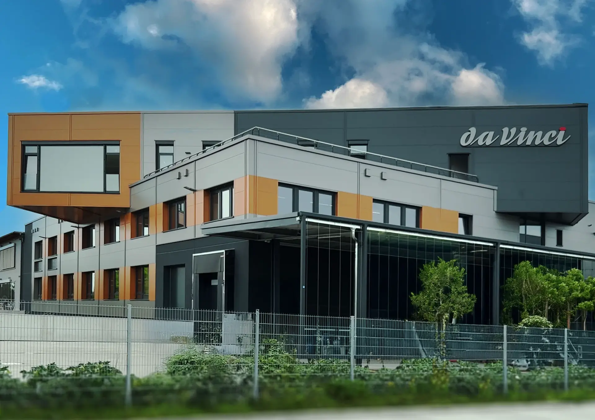 Ein modernes Gebäude mit orangen und grauen Akzenten, oben rechts ist das Logo von da Vinci Künstlerpinsel am Gebäude angebracht