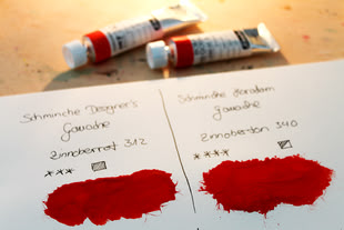 Schmincke Gouache, Foto: Farbensammler.de Zwei rote Gouache-Farben von Schmincke im Vergleich, mit Farbproben auf Papier und Tuben im Hintergrund.