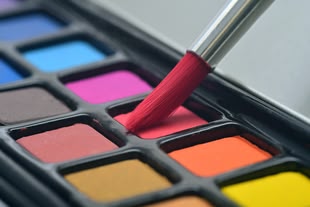 Nahaufnahme eines Aquarellkasten mit einem Pinsel.
