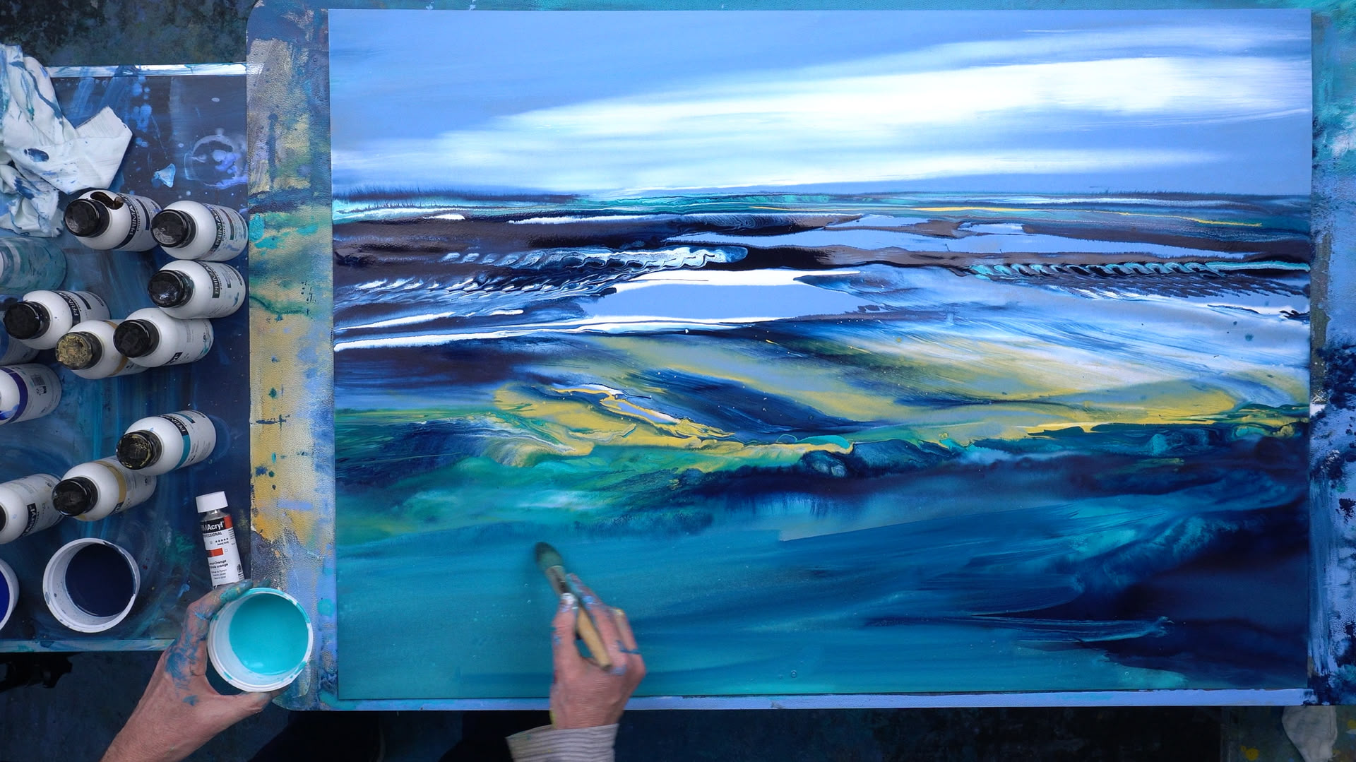 Blick aus der Vogelperspektive auf ein abstraktes Acrylwerk mit dem Meer als Motiv, an dem der Künstler (Hinrich Schüler) gerade mit einem Pinsel in der Hand arbeitet.