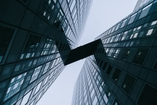 Moderne Architektur fotografieren lernen im Fotokurs oder Fotoworkshop. Foto: John Towner/Unsplash. Zwischen zwei Hochhäusern befindet sich ein Übergang. Die Fotografie wird in der Froschperspektive dargestellt.