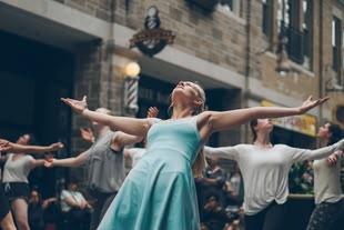 Geben Sie Ihren Fotos Tiefe! Fotografieren lernen im Fotokurs. Foto: Nadim Merrikh/Unsplash. In einer Straße stehen mehrere Tänzer mit dem Blick nach oben gerichtet.