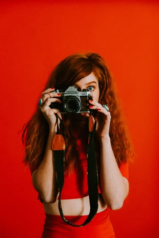 Nicht immer nur durch den Sucher schauen! Foto: Jordan Whitfield/Unsplash. Eine in rot gekleidete Frau vor einem roten Hintergrund.