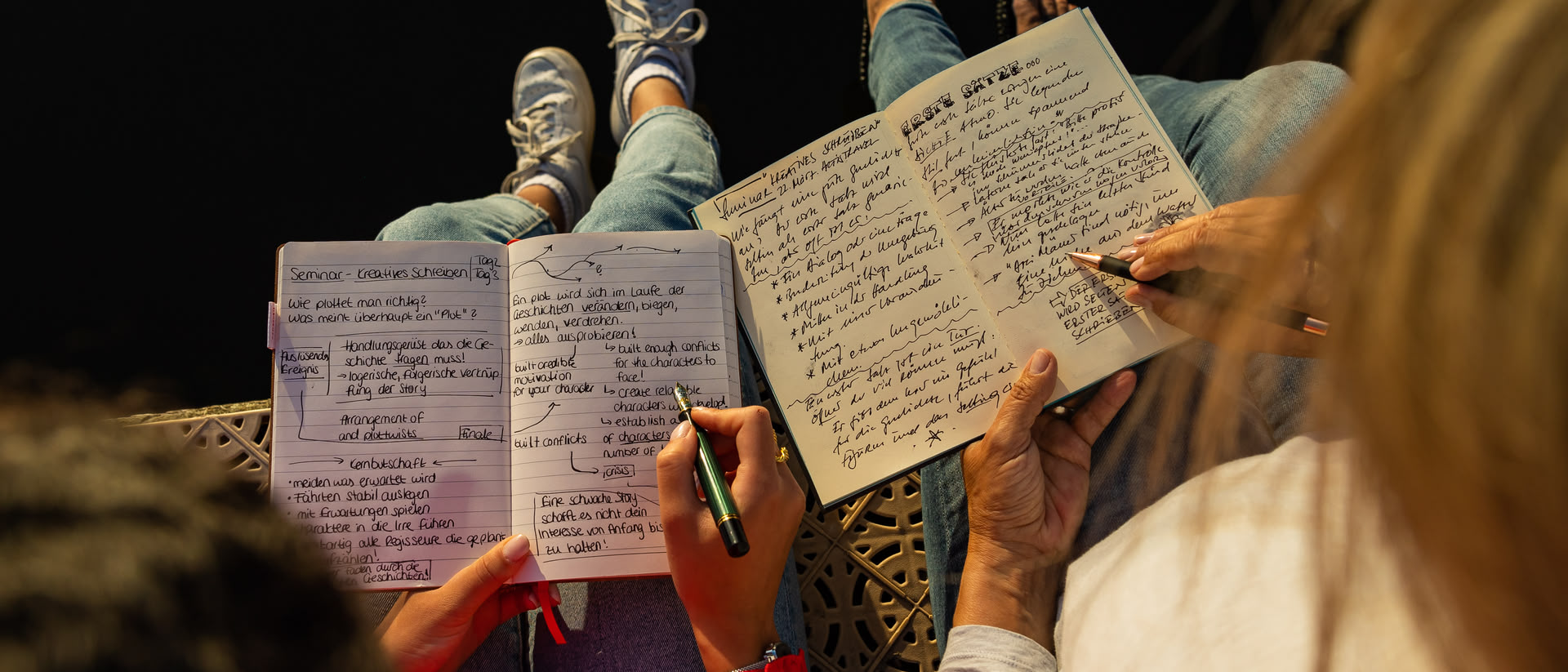 Blick von oben auf die offenen Notizbücher von zwei Personen, die an einem Seeufer sitzen