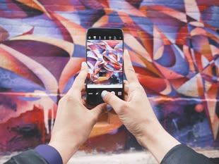 Zwei Hände halten ein Handy, mit dem eine bunte Wand fotografiert wird.