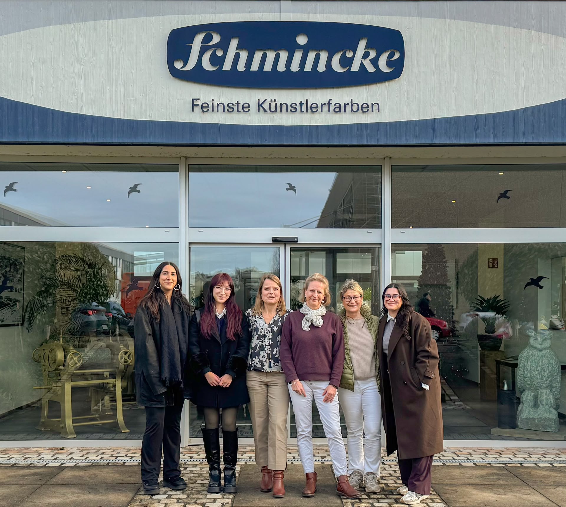 6 Frauen stehen nebeneinander vor dem Eingang des Werks der Firma Schmincke Feinste Künstlerfarben