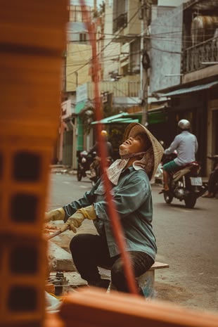 Menschen fotografieren lernen im Fotokurs: Reisefotografie. Foto: Tayla Linford/Unsplash. Die Fotografie stellt eine Frau da, die in einer Straße sitzt und am arbeiten ist.