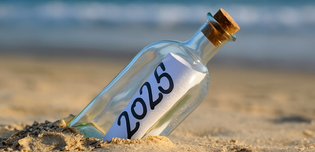 Flaschenpost steckt im Sand eines Strandes, darin ein Zettel mit der Aufschrift "2025"