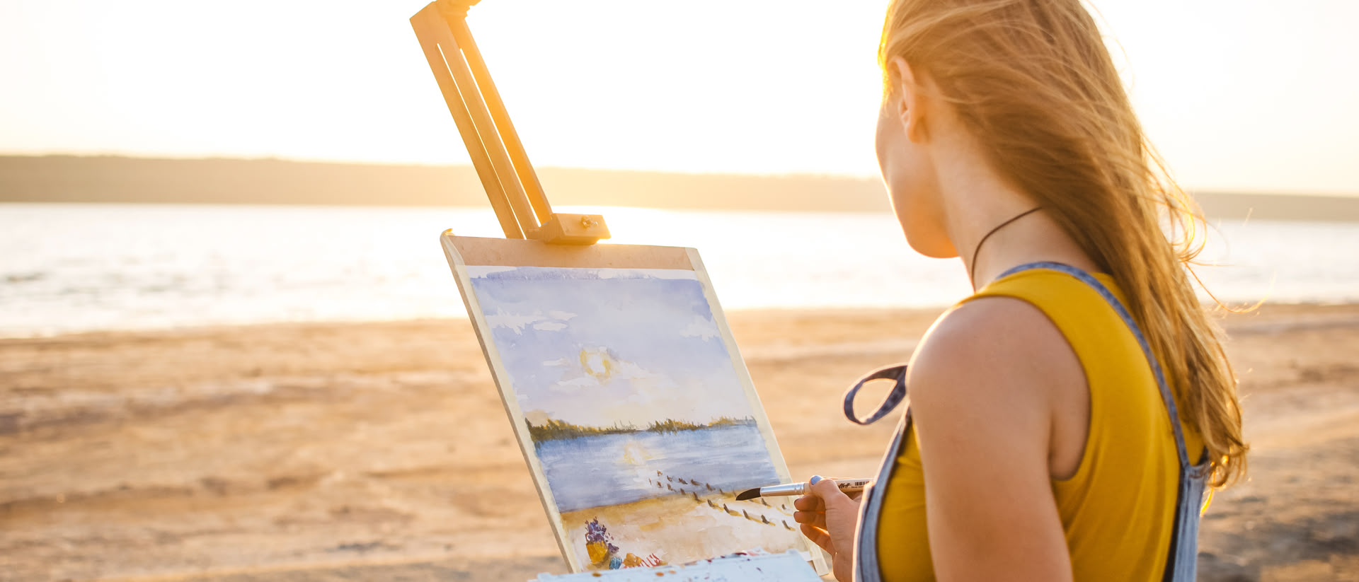 Eine Frau steht vor einer Leinwand am Strand eines Sees und malt ihren Ausblick