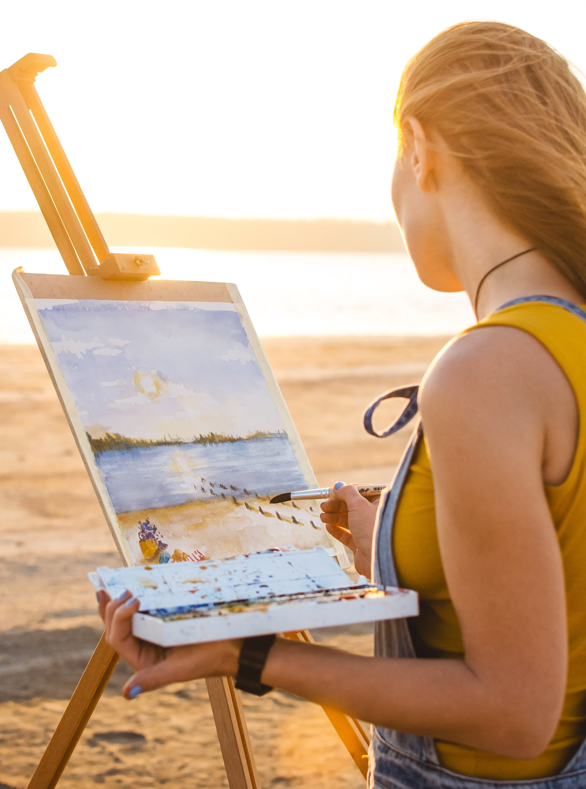 Eine Frau steht vor einer Leinwand am Strand eines Sees und malt ihren Ausblick